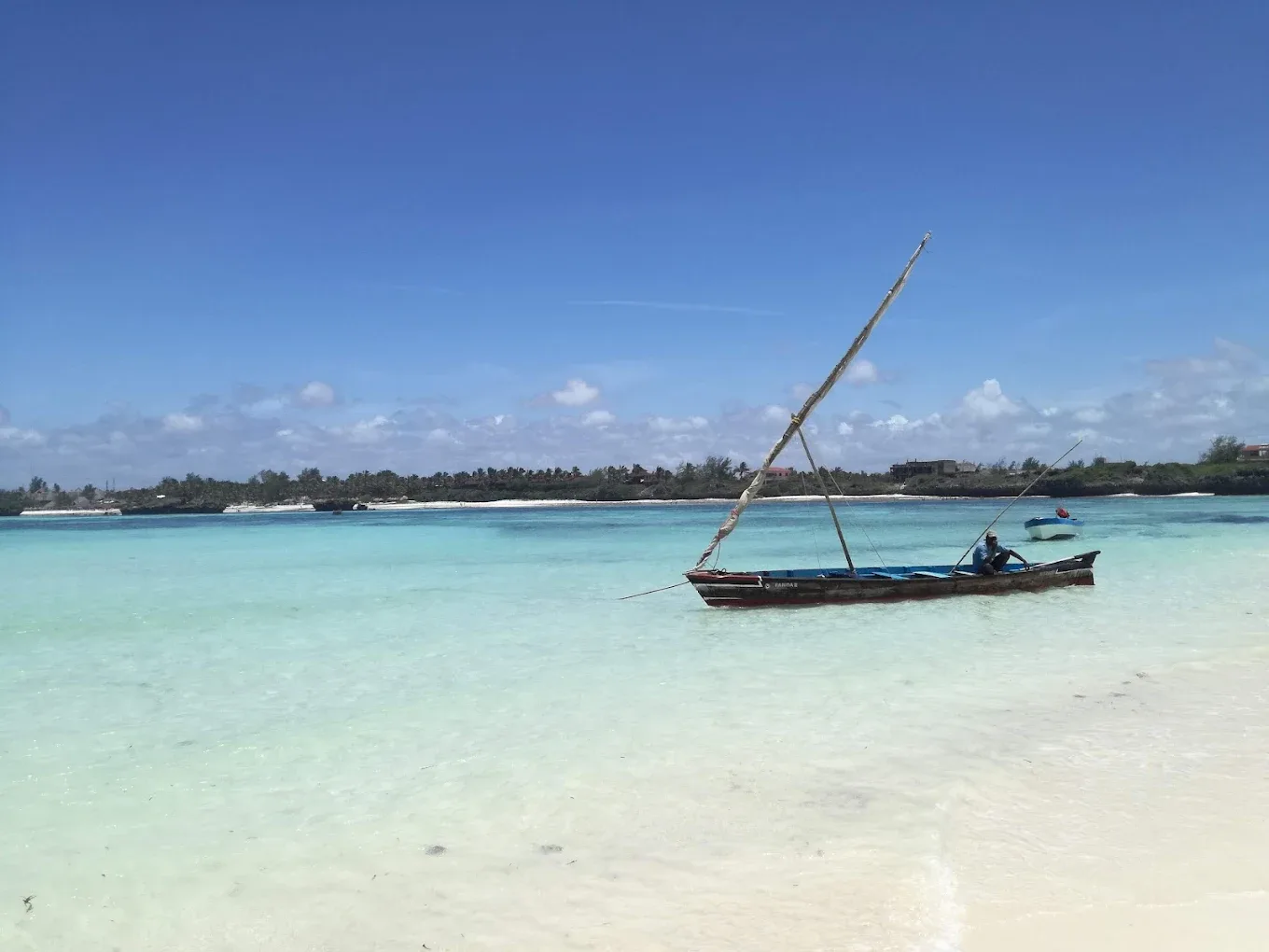 Traditional dhow sailboat in turquoise shallow waters near white sandy beach